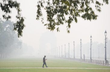A pedestrian walks wearing a mask amid dense smog