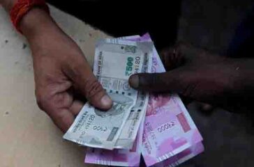 A customer hands Indian currency notes to an attendant at a fuel station in Mumbai