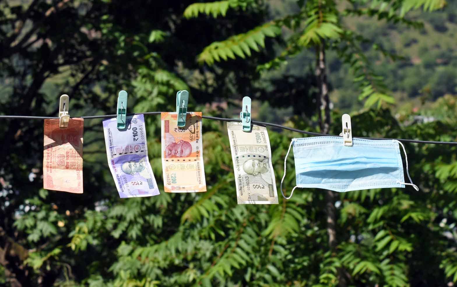 Indian currency notes and a mask clipped with a rope for dry in the sun