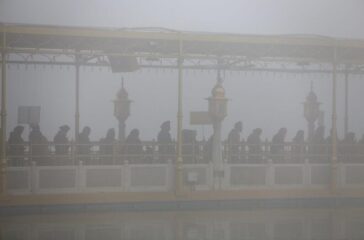 Devotees stand in a queue on the path towards the Golden Temple amid dense fog